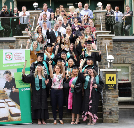 Cambrian apprenticeship graduates standing outside with their cap and gowns and certificates