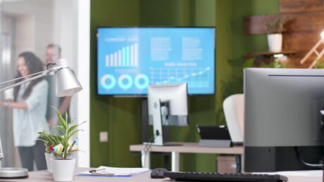 Empty startup business company office with nobody in it having monitor with management graphs on it ready for financial presentation. Workplace with paperworks on desk table, modern furniture