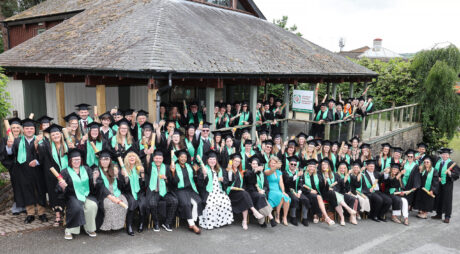 Learners sitting outside with their caps and gowns, raising a celebratory drink.